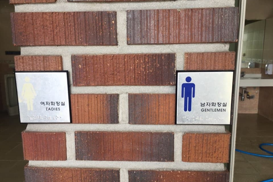 Accessible restroom 0 : Restroom information signs with Korean, pictograms, and braille attached on a red brick wall