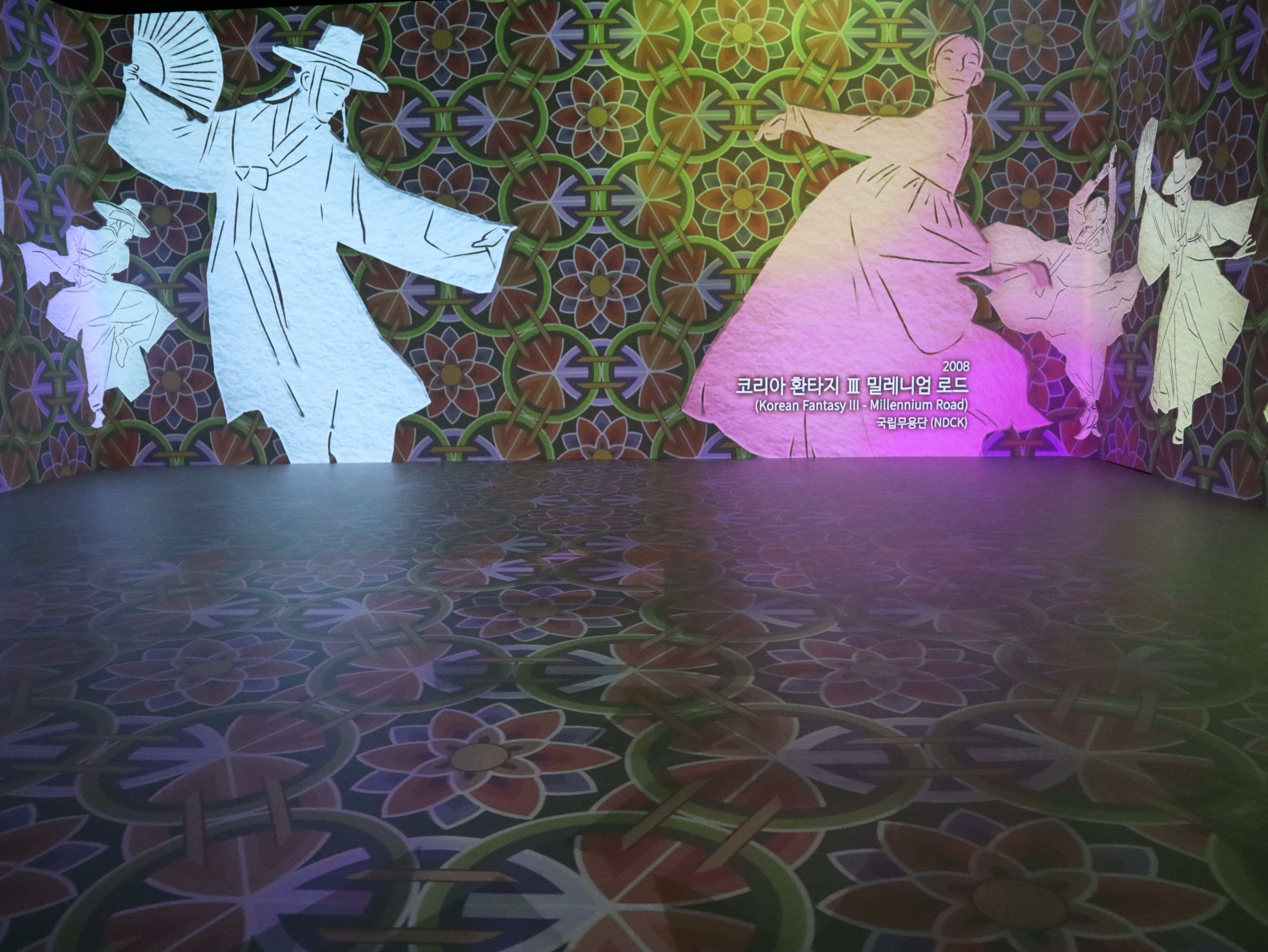 국립극장2 : 바닥과 벽 전체에 비추는 단청 바탕 무늬 위로 춤을 추는 한복을 입은 남녀가 보이는 미디어 아트 작품