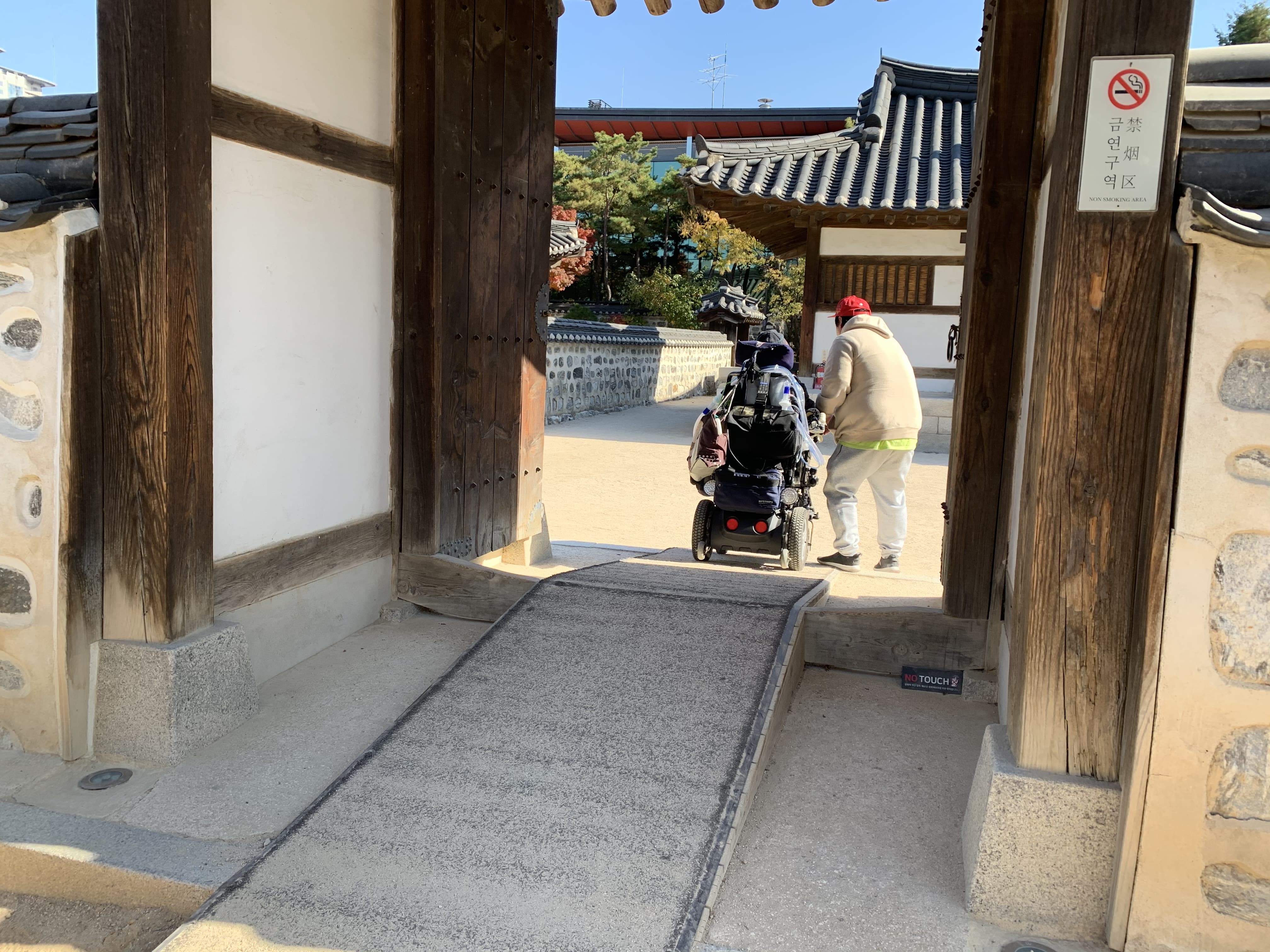 이동로0 : 전통가옥 대문 출입구에 설치된 긴 경사로를 지나가는 휠체어 사용자와 동반자