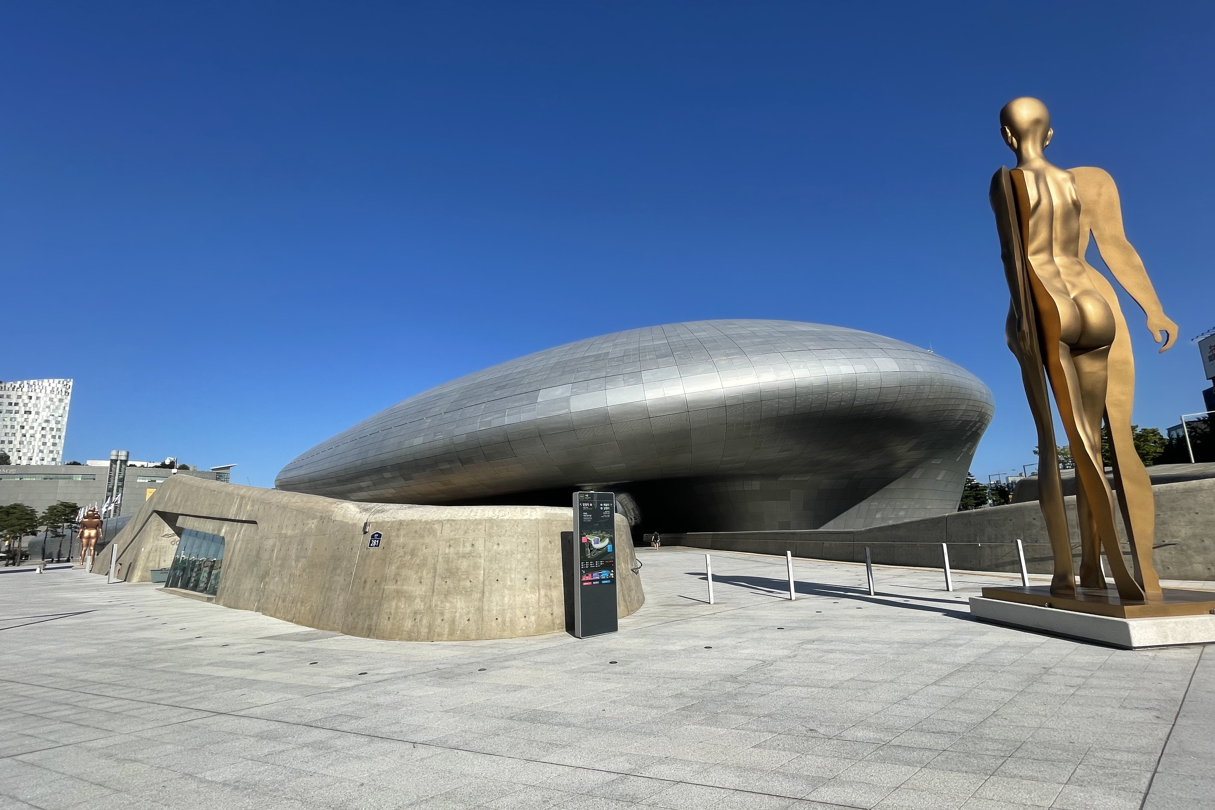 Dongdaemun Design Plaza (DDP)1 : Exterior view of entire Dongdaemun Design Plaza and entryway where one can see human-shaped sculpture 
