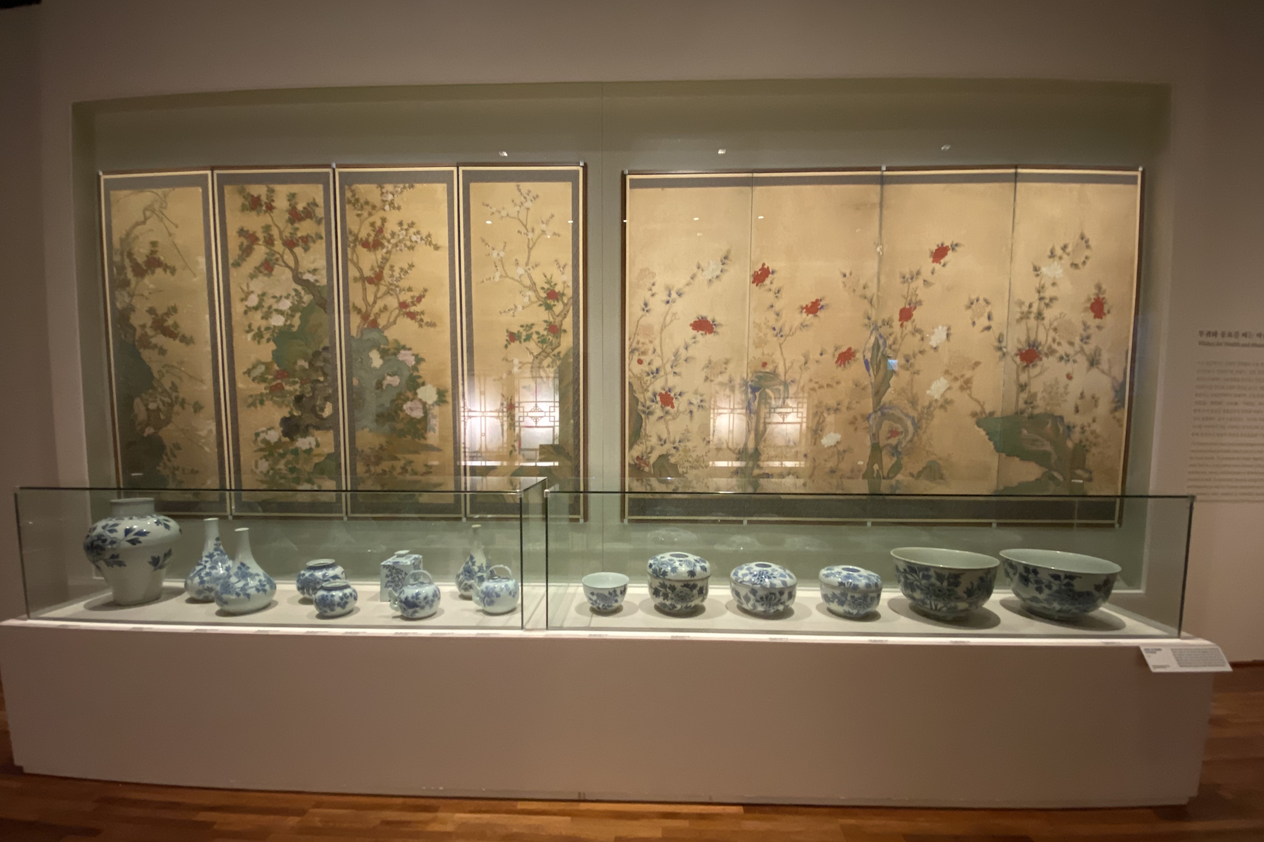 National Palace Museum of Korea1 : An exhibition hall with pottery displayed on a glass display stand in front of a folding screen with flower paintings

