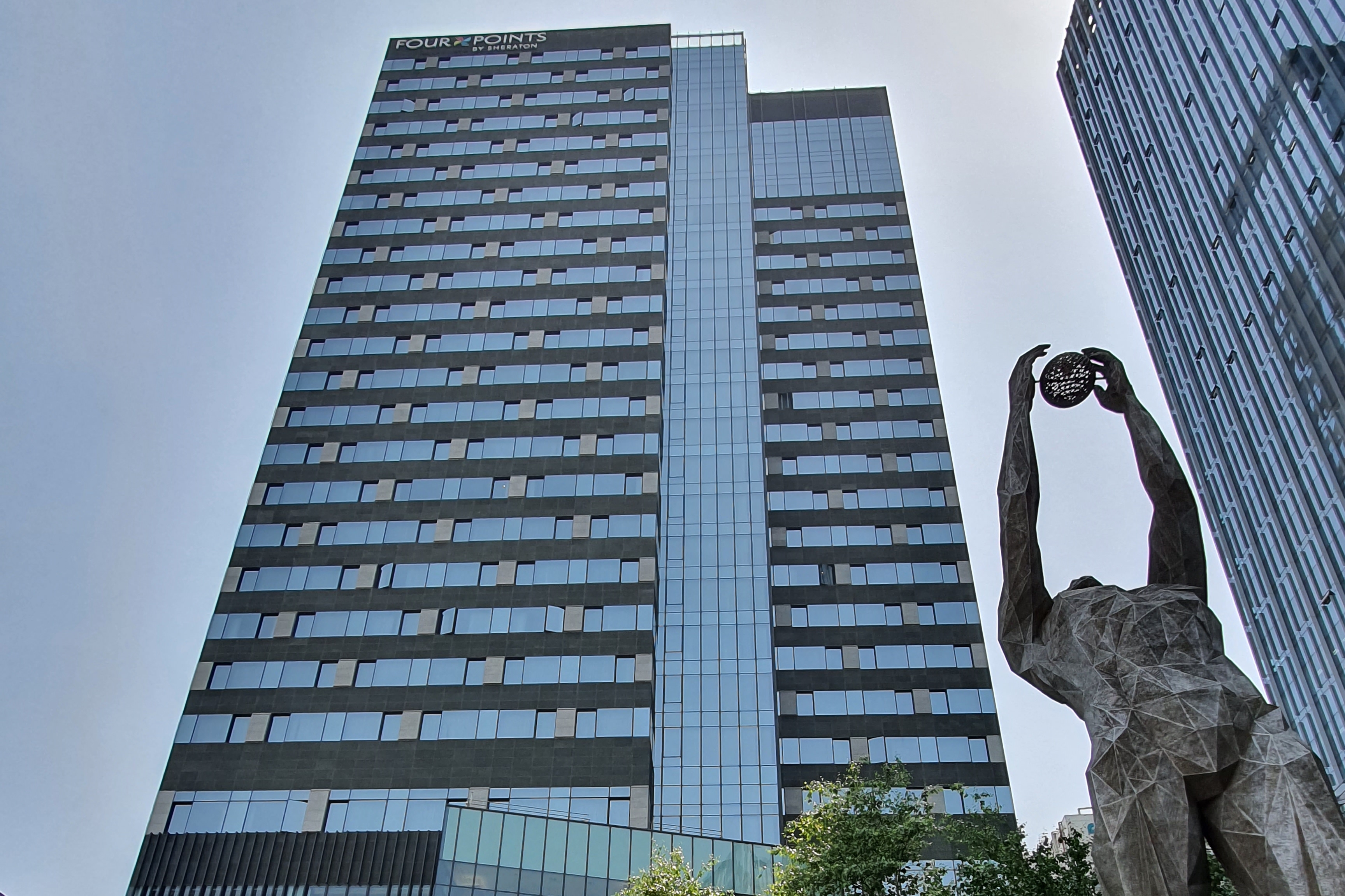 Four Points by Sheraton Josun, Seoul Myeongdong0 : Exterior view of the hotel building in the center and a full body figure with arms outstretched on the right