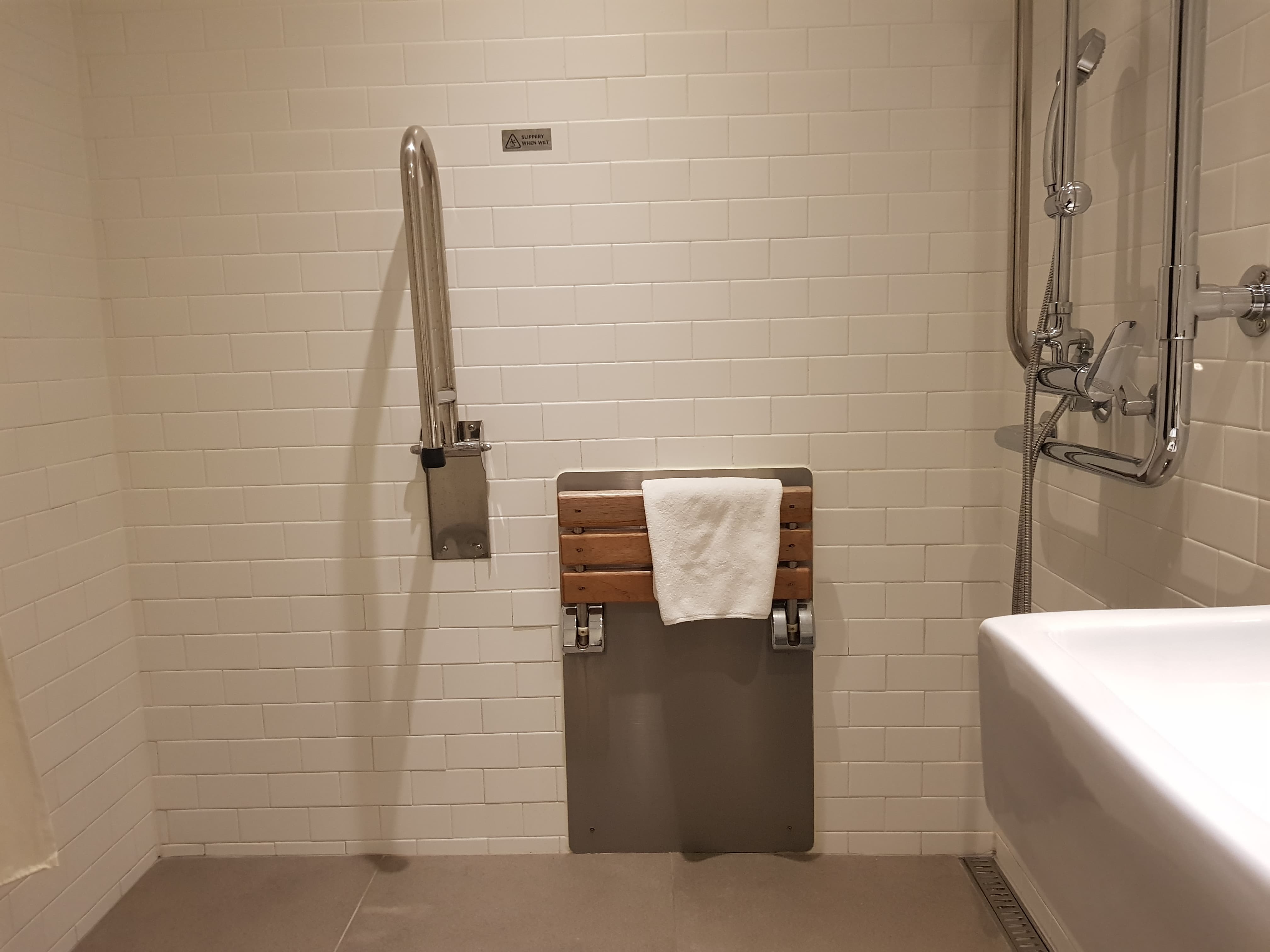Accessible guestroom bathroom0 : Wall-mounted shower chair with a towel hanging over