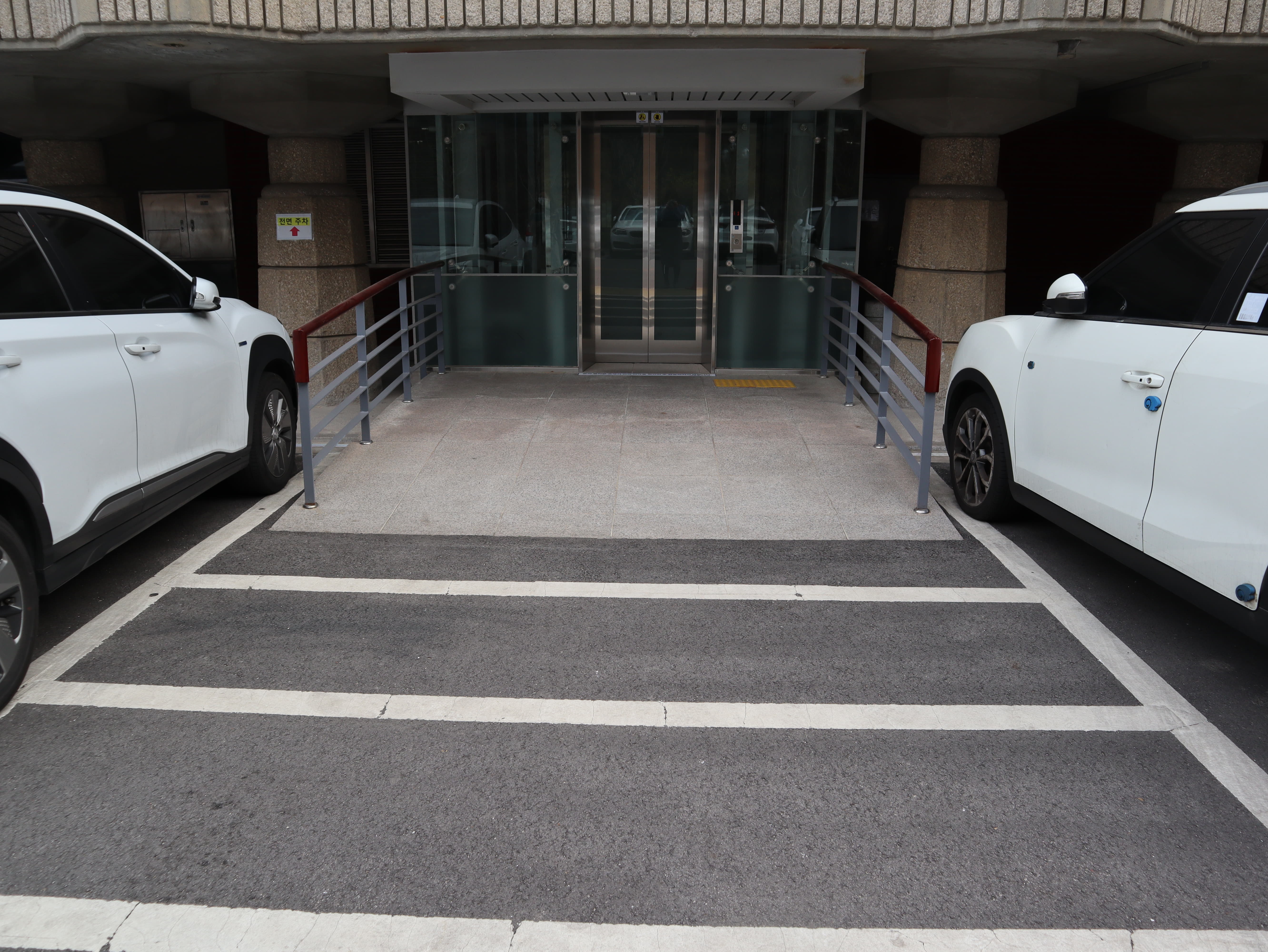 달오름극장 편의시설0 : 흰색 차 두 대 사이로 보이는 건물 출입용 엘리베이터와 연결된 접근로